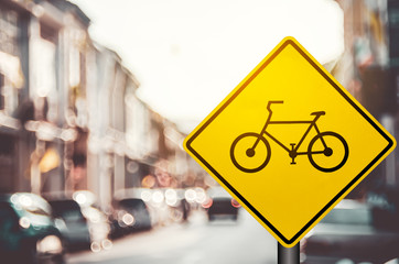 Bicycle warning sign on blur traffic road with colorful bokeh light abstract background.