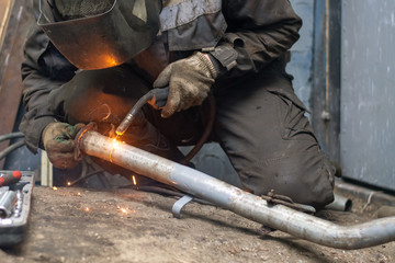 repairing of corrugation muffler of exhaust system in car workshop - serviceman welds the old...