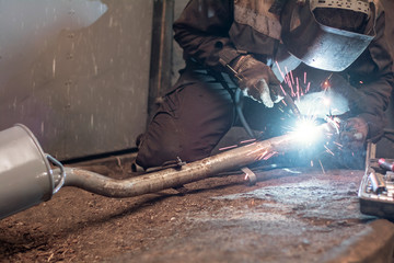repairing of corrugation muffler of exhaust system in car workshop - serviceman welds the old...