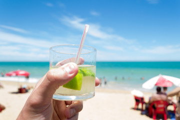 Relax time at the beach in Marataizes, a little seaside village in the Espirito Santo state in Brazil. A hand holding a caipirinha a typical local drink