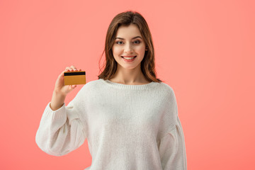 smiling brunette girl holding credit card isolated on pink