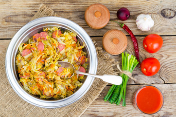 Fried sauerkraut with sausages in metal bowl.