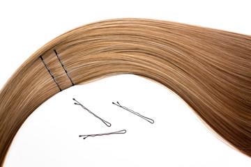 Piece of beautiful, shiny blonde hair on white isolated background with bobby pins. Wavy shape