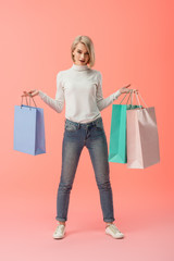 attractive blonde young woman holding shopping bags on pink background