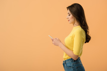 Side view of pretty brunette girl using smartphone isolated on orange