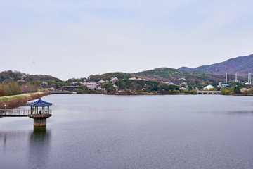A view of blue roof gazebo on a lake and  mountains with cherry blossoms.