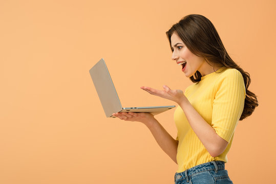 Emotional Brunette Young Woman Holding Laptop Isolated On Orange