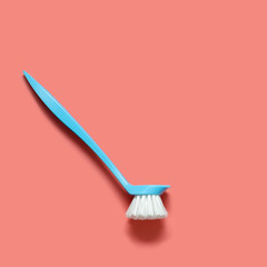 Pale blue brush for washing dishes lying on living coral background. In the style of pop art. Top view. Copy space.