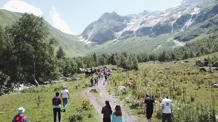 Aerial shooting from flying drone hiking group walking on mountain trail. Tourist group traveling in mountain valley. Hiking tour in mountain. Traveling group walking on mountain trail aerial view