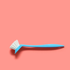 Pale blue brush for washing dishes lying on living coral background. In the style of pop art. Top view. Copy space.