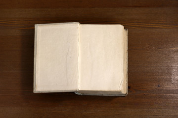 An open old retro book with white blank empty pages on which the designer can write a greeting text or a postcard on the wooden background of the library atmosphere
