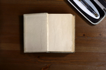 An open old retro book with white blank empty pages next to pen on which the designer can write a greeting text or a postcard on the wooden background of the library atmosphere