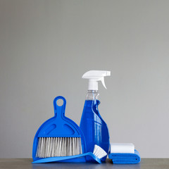 Fototapeta na wymiar Blue cleaning kit on neutral background: Spray detergent, dishwashing brush, dust cloths, sponge, scoop and broom. Copy space.