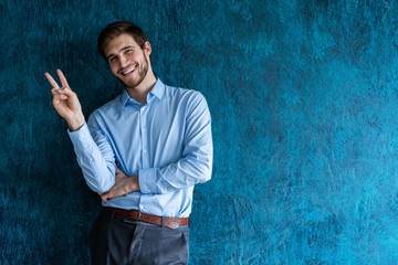 business man in a suit giving the victory sign on blue background.