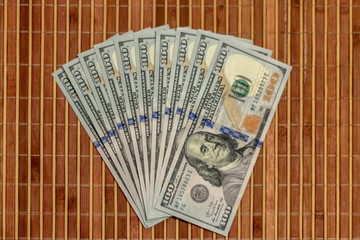 The stack is 100 dollar bills USD spread out like a fan, on a wooden background.