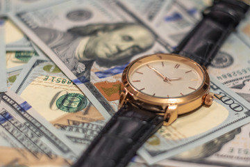 Wrist gold watch lie on the bills of 100 dollar money. Soft focus.