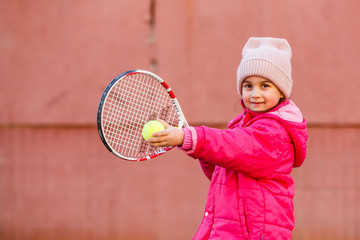 Little Girl learning to hit the tennis ball. Little girl tennis player with ball and racket on court. Active exercise for kids