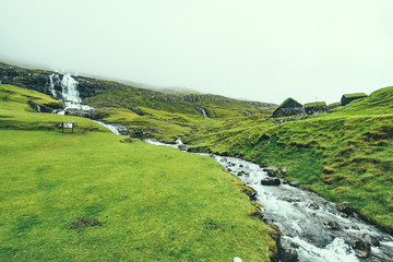 Fototapeta na wymiar Beautiful peaceful rock house with green grass on the roof in Saksun valley next to the waterfall in foggy weather, Faroe Islands, North Europe, hidden gem for travel destination