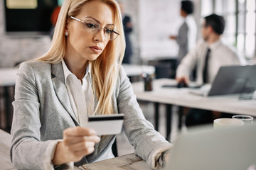 Businesswoman holding credit card while using laptop and e-banking at work.