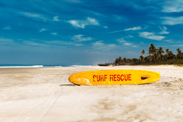 Bright yellow surfboard in the form of a pointer with a red word rescue on a sandy beach in the...