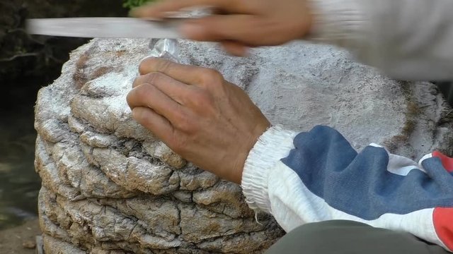 Close up of craftsman hands rasping stone statuette of a cat outdoors on a trunk of palm tree outdoors in Morocco