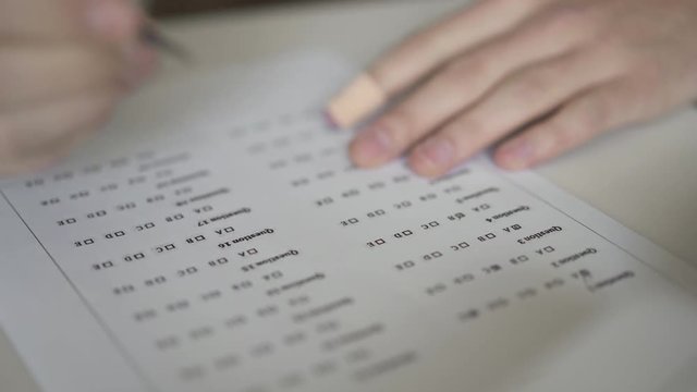 Close up of male hand and a blank with multiple choice quiz. Close up of hand painting a cell with answers in multiple-choice questions. Student fills in answers in multiple choice test