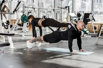 Athletic couple doing difficult sport exercise where the girl stands in the plank on a man who stands in the plank in the modern gym