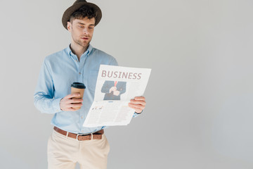 handsome man reading business newspaper and holding paper cup isolated on grey