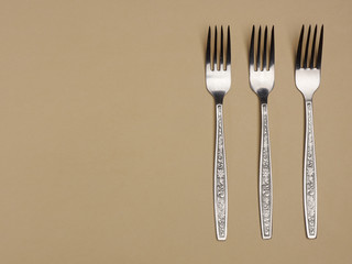 Three stainless steel fork, spoon and knife on a yellow background with copyspace