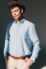 handsome man in blue shirt and brown hat standing in sunlight