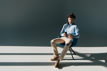 handsome man with smartphone and paper cup sitting on chair