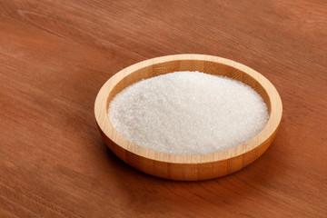 A bowl of white sugar on a dark rustic wooden background with copy space