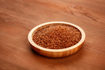 A bowl of brown cane sugar on a rustic wooden background with a place for text