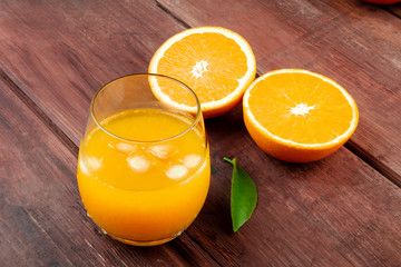 A glass of fresh orange juice with orange halves and a green leaf on a dark rustic wooden background with a place for text