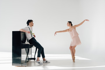 Obraz premium handsome musician standing by piano and looking at beautiful ballerina dancing