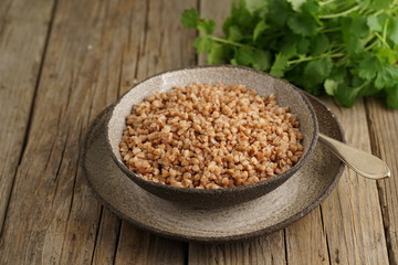 Boiled buckwheat porridge in black bowl and spoon on dark old wooden background, side view