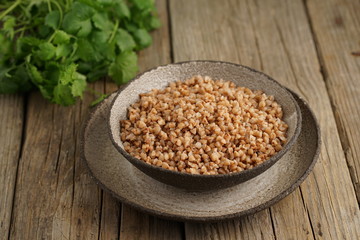 Boiled buckwheat porridge in black bowl on dark old wooden background, side view