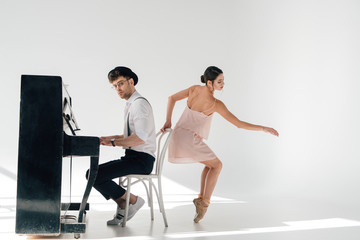 Obraz premium handsome pianist playing piano while graceful ballerina dancing near his chair