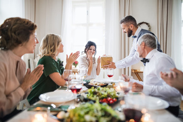 A man giving gift to a young surprised woman on a family birthday party.