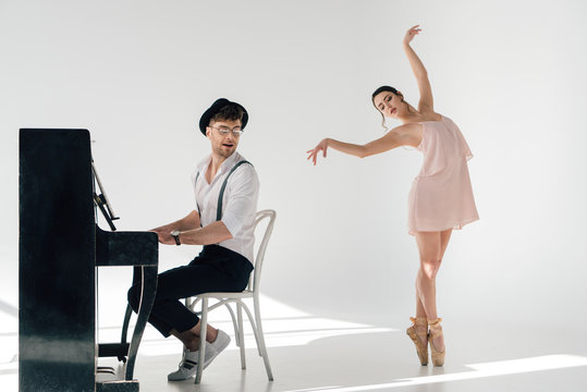 musician playing piano while attractive ballerina dancing near him