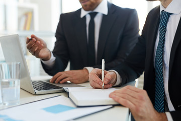 One of young contemporary office managers making notes in notebook while listening to presentation of colleague