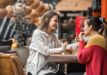 Two happy women are sitting in a cafe, drinking milkshakes,