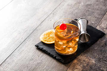 Old fashioned cocktail with orange and cherry on wooden table. Copyspace