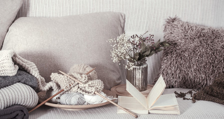 Vintage wooden knitting needles and threads on a cozy sofa with pillows and a vase of flowers. Open book for reading