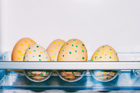 Easter eggs with pattern of yellow and green dots in plastic tray in fridge with copy space closeup