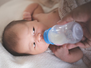 Close up of Asian female newborn baby lying in bed and Suck milk Bottle in home with sunlight in the morning. Cute little girl three weeks old. Baby health concept