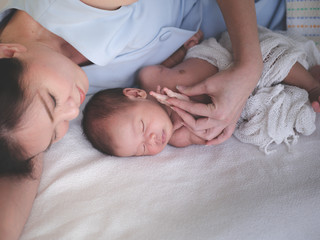 Fototapeta na wymiar Mother take care of Asian female newborn baby lying in bed and sunlight in the morning. Cute little girl three weeks old. Healthcare, love, relationship concept