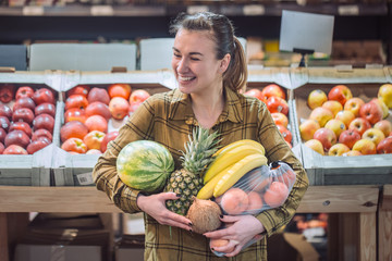 Fototapeta premium Woman in the supermarket. Beautiful young woman shopping in a supermarket and buying fresh organic vegetables