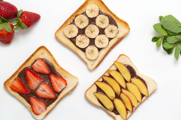 Tasty toast bread with chocolate paste, banana, strawberry and peach on white background.