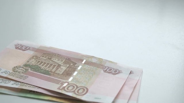 To count money. Money falls on a white table. People hand quickly throws russian rubles banknotes nominals 200 and 100 and coins nominal 10 on a white background